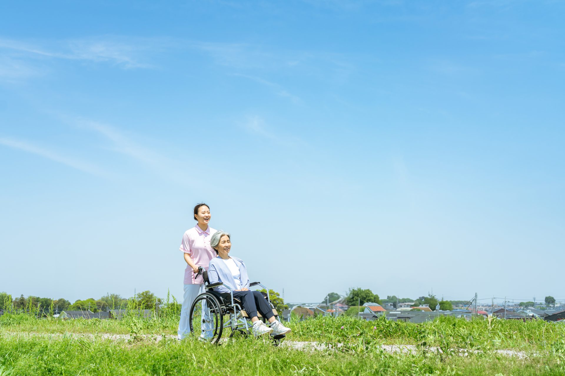 菜の花畑と車椅子を押す介護スタッフ